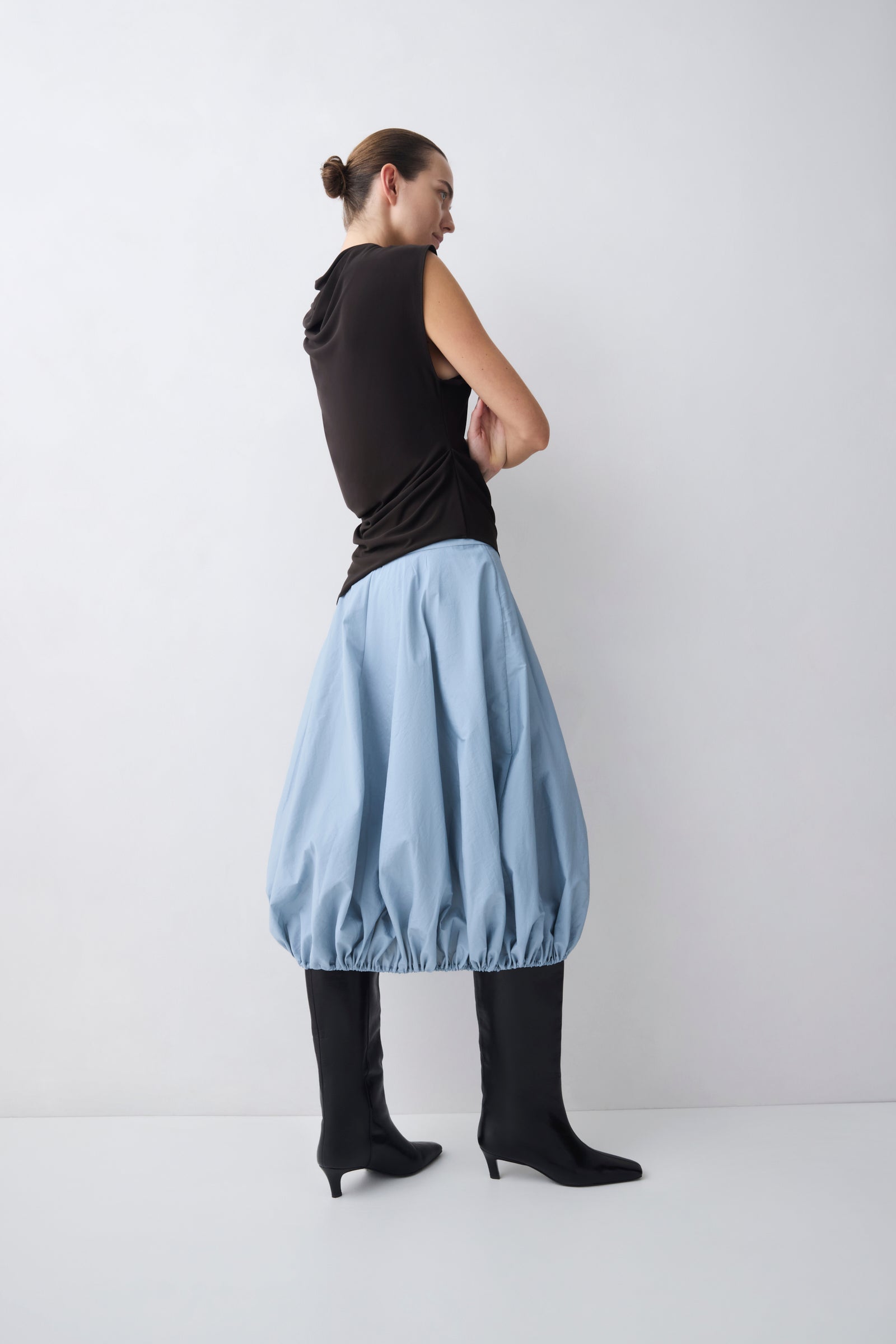 Woman wearing a brown sleeveless top and light blue skirt on a white background