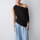 Woman wearing a brown one-shoulder top and light blue harem pants against a white background
