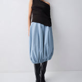 Person wearing a brown sleeveless top and blue skirt with black boots on a white background