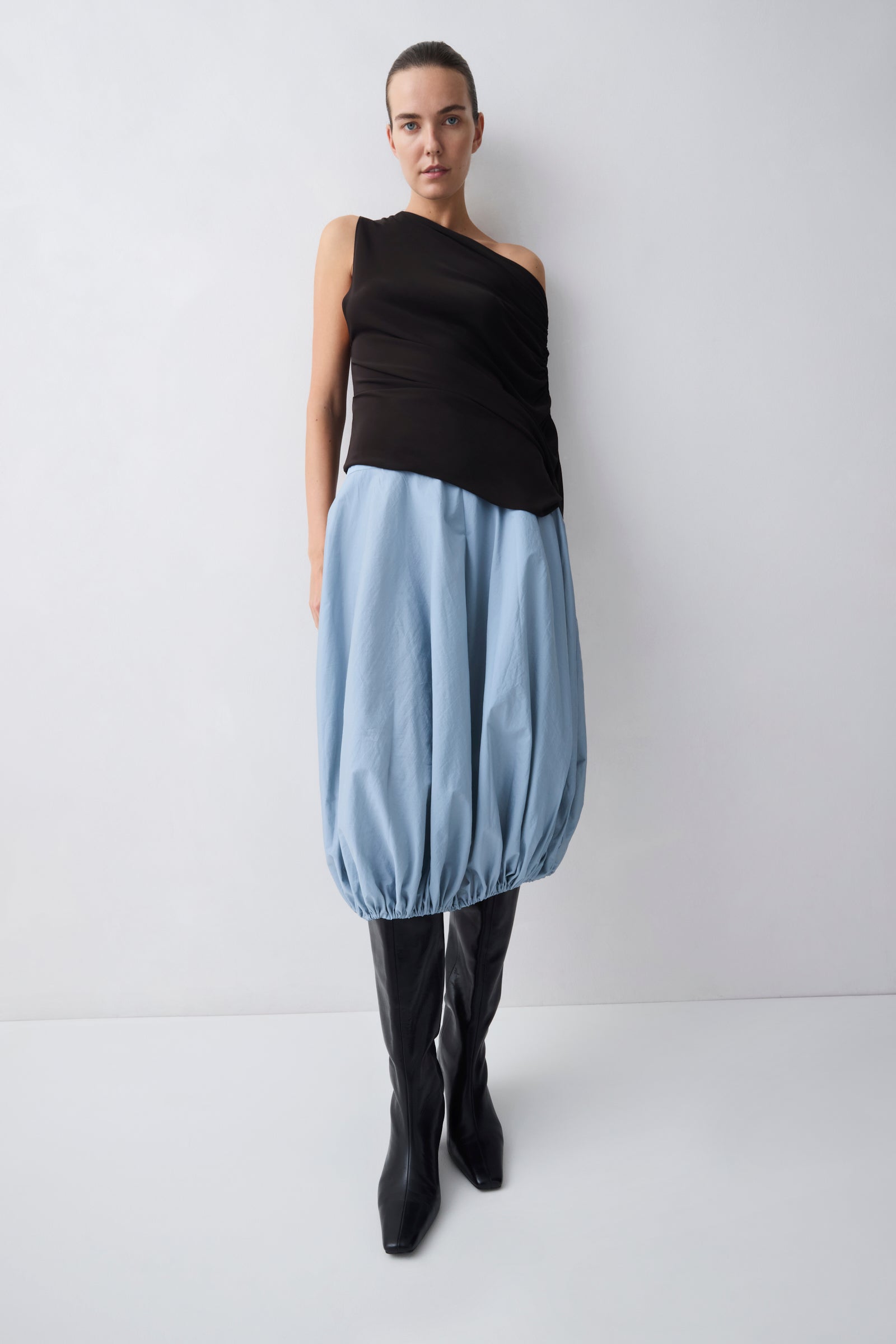 Person wearing a brown sleeveless top and blue skirt with black boots on a white background
