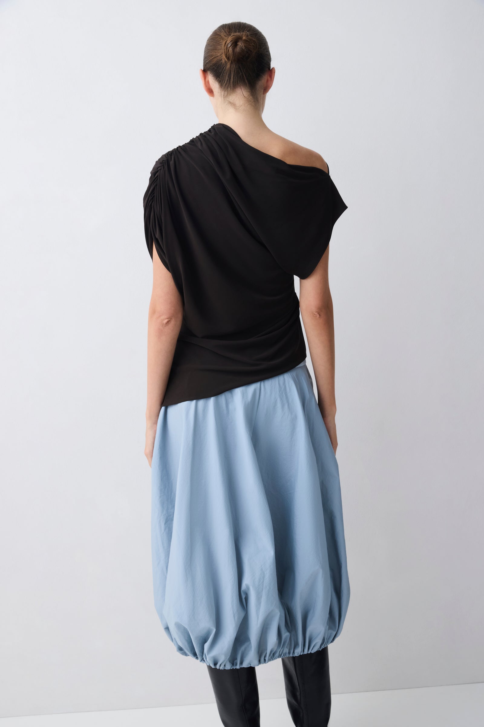 Person wearing a brown one-shoulder top and light blue skirt on a white background
