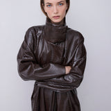 A model wearing a dark brown textured faux-leather wrap coat with a high collar and long sleeves, standing against a light gray background.