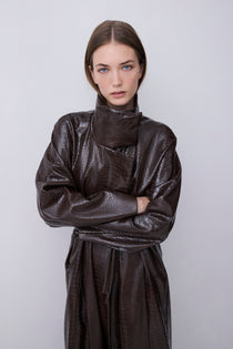 A model wearing a dark brown textured faux-leather wrap coat with a high collar and long sleeves, standing against a light gray background.