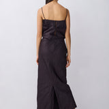 A woman viewed from the back wearing a black spaghetti-strap maxi dress with a gathered bodice and wide-leg skirt, paired with black heeled sandals, against a light gray studio background.