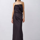 A model wearing a black draped spaghetti-strap maxi dress with a gathered waist, paired with black thong sandals, against a light gray studio background.