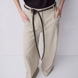 A person wearing beige wide-leg trousers with a dark brown rope belt tied at the waist, paired with a black sleeveless top, against a plain light gray studio background.