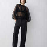 Person wearing a black sheer top and black pants on a white background