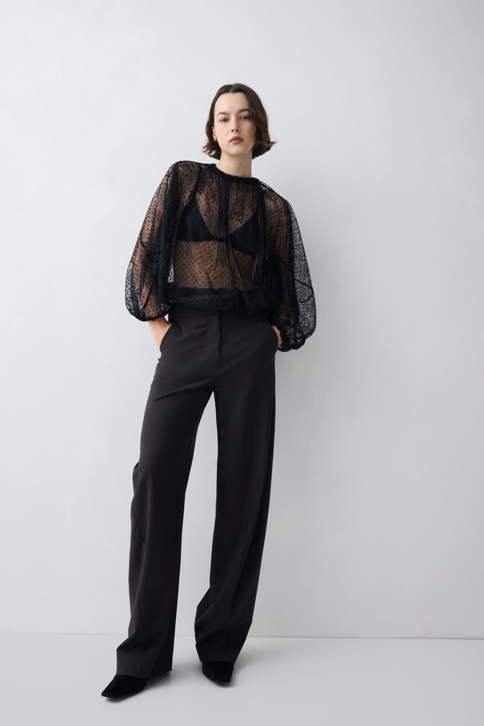 Person wearing a black sheer top and black pants on a white background