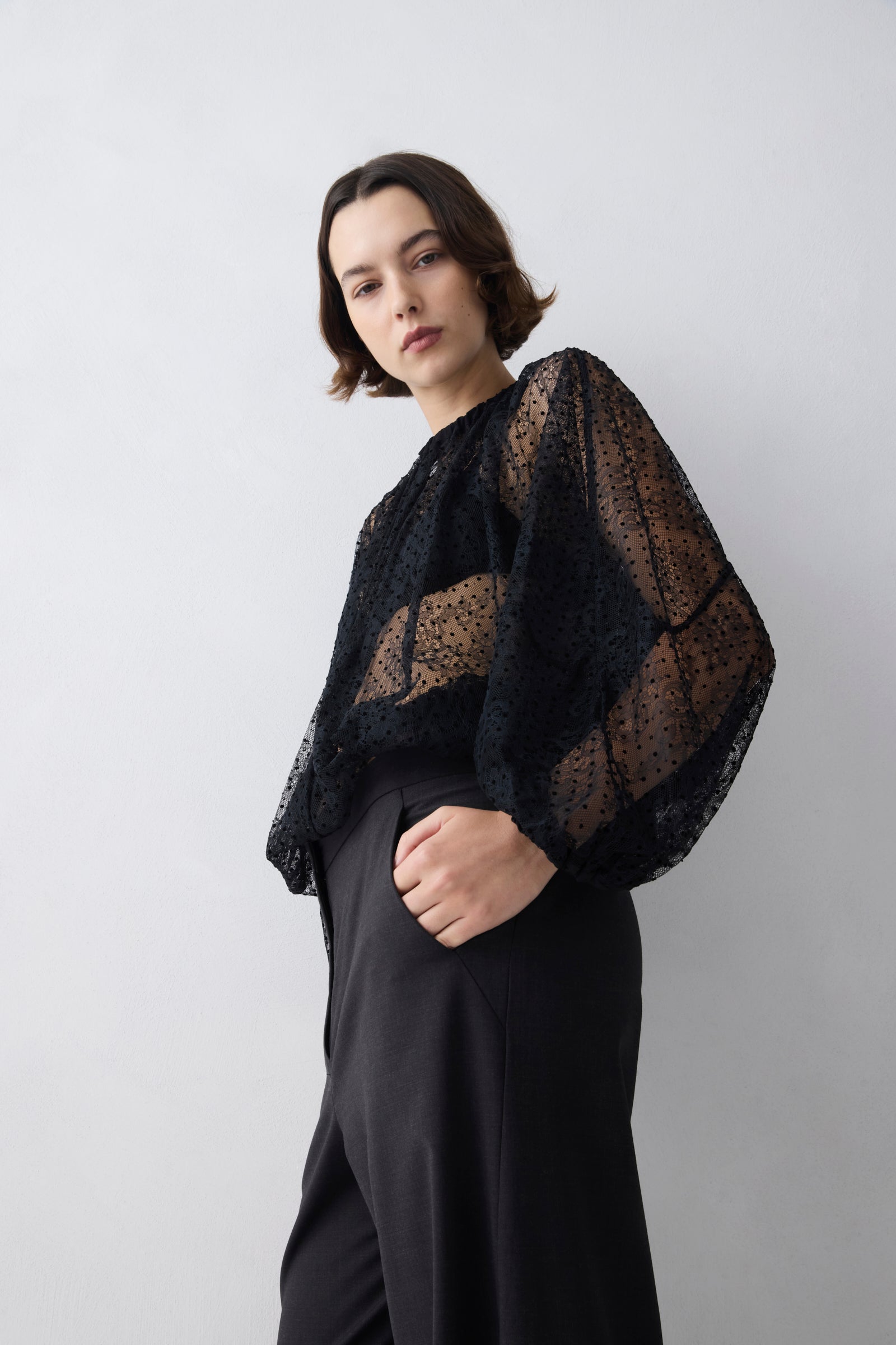 Woman wearing a black lace top against a plain background