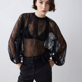 Person wearing a black sheer blouse with puffed sleeves against a white background