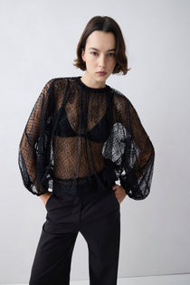 Person wearing a black sheer blouse with puffed sleeves against a white background
