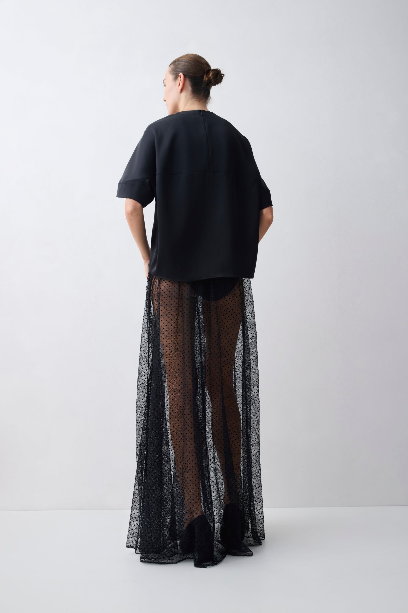 Person wearing a black outfit with a sheer black skirt on a white background