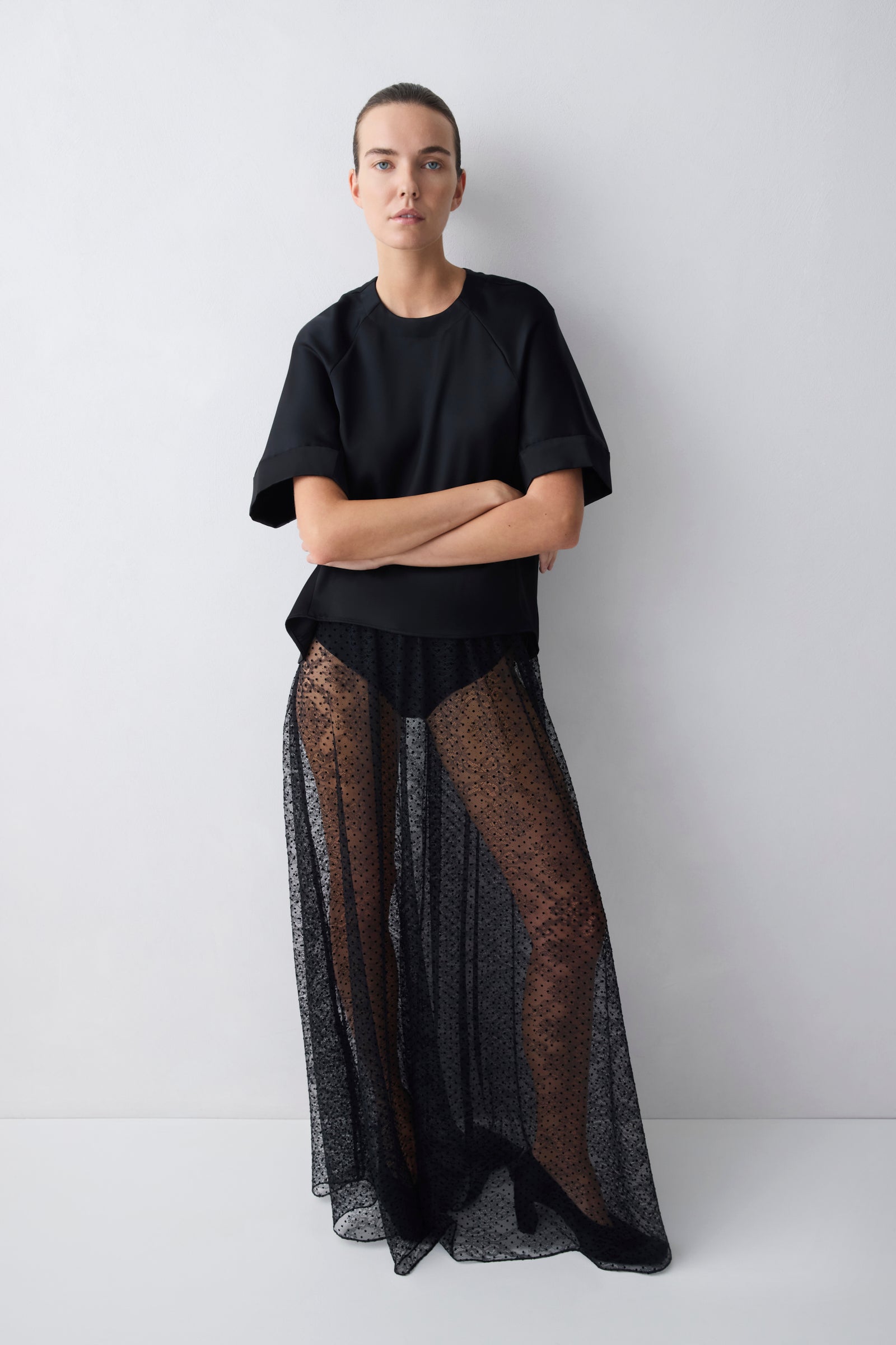 Person wearing a black outfit with sheer overlay on a white background