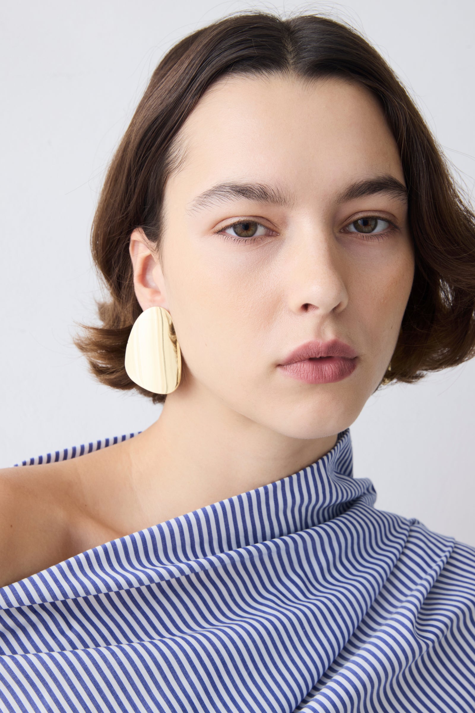 Woman wearing large beige earrings against a plain background