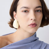 Woman wearing large beige earrings against a plain background