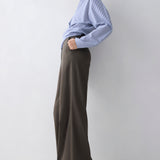 Person wearing a light blue shirt and brown wide-leg pants against a white background