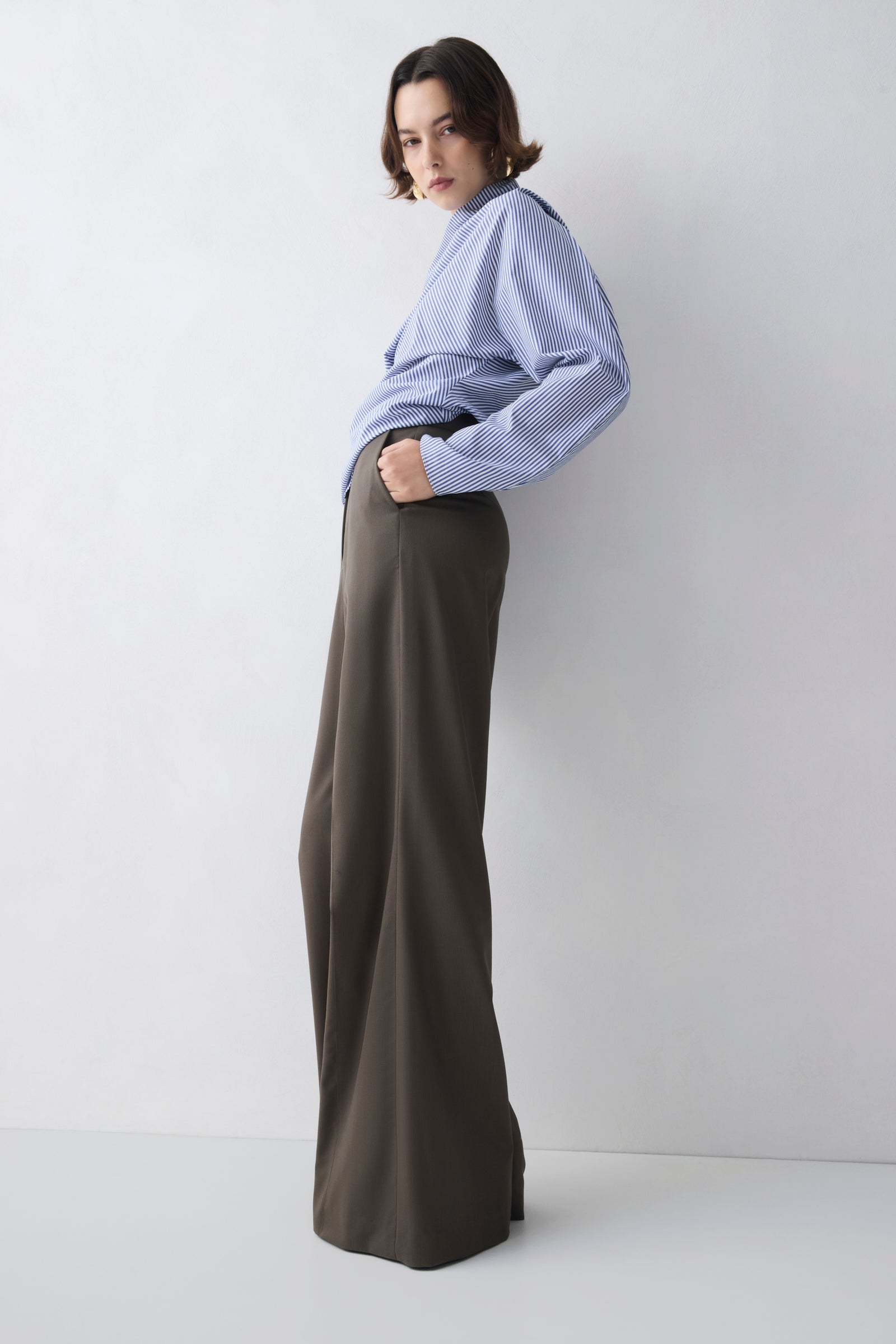 Person wearing a light blue shirt and brown wide-leg pants against a white background