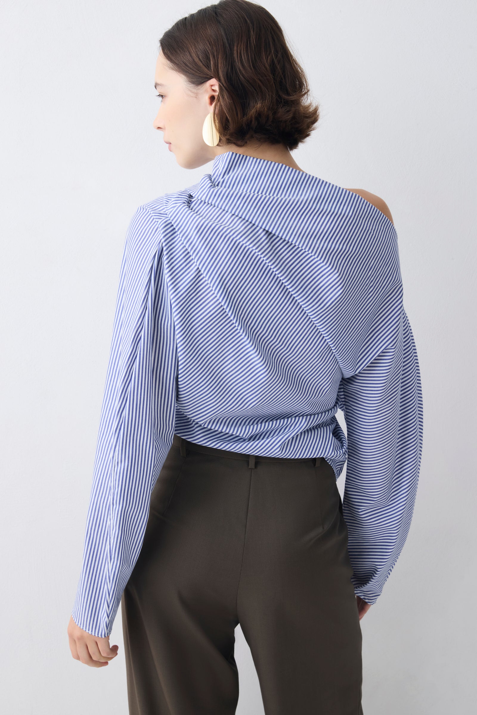 Woman wearing a blue and white striped blouse with a high collar against a plain background