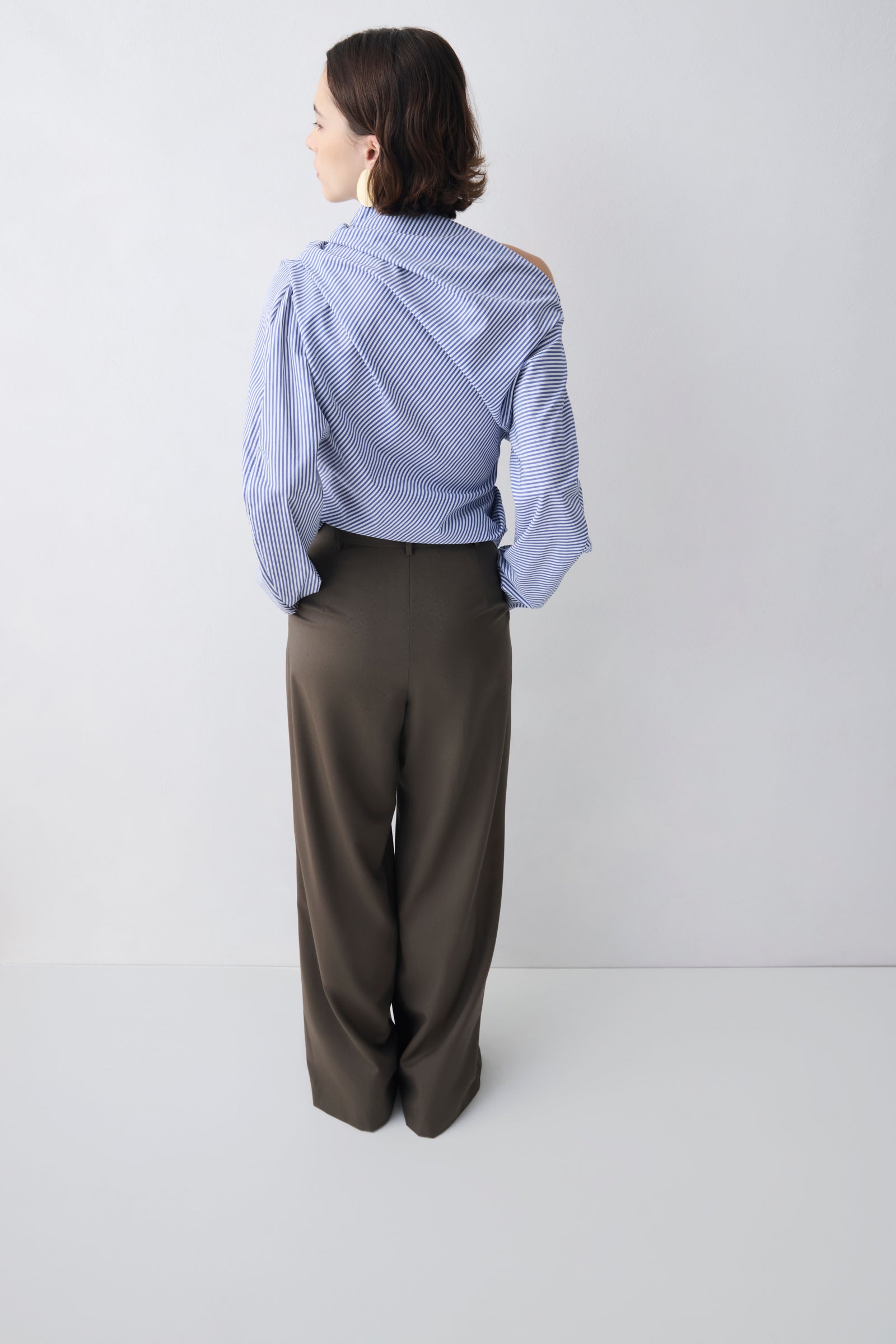 Person wearing a light blue striped shirt and dark green pants on a white background