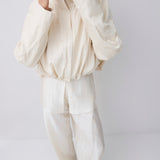 A model wearing a cream-colored, textured two-piece outfit consisting of a cropped zip-up jacket and matching wide-leg trousers, photographed against a neutral light gray background.