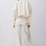 A model shown from the back wearing a cream-colored textured jacket and matching wide-leg trousers against a plain white studio background.