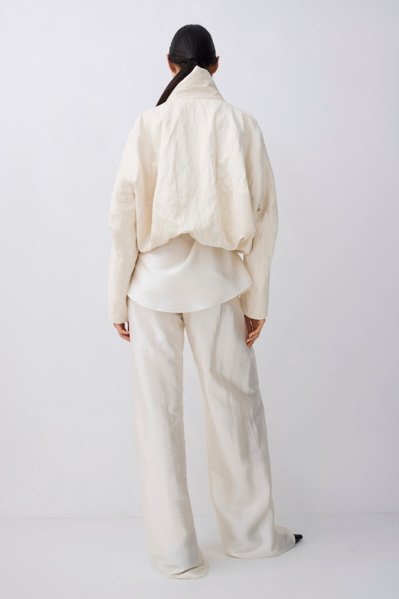 A model shown from the back wearing a cream-colored textured jacket and matching wide-leg trousers against a plain white studio background.