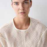 Woman wearing a beige sweater with a wavy pattern against a light background
