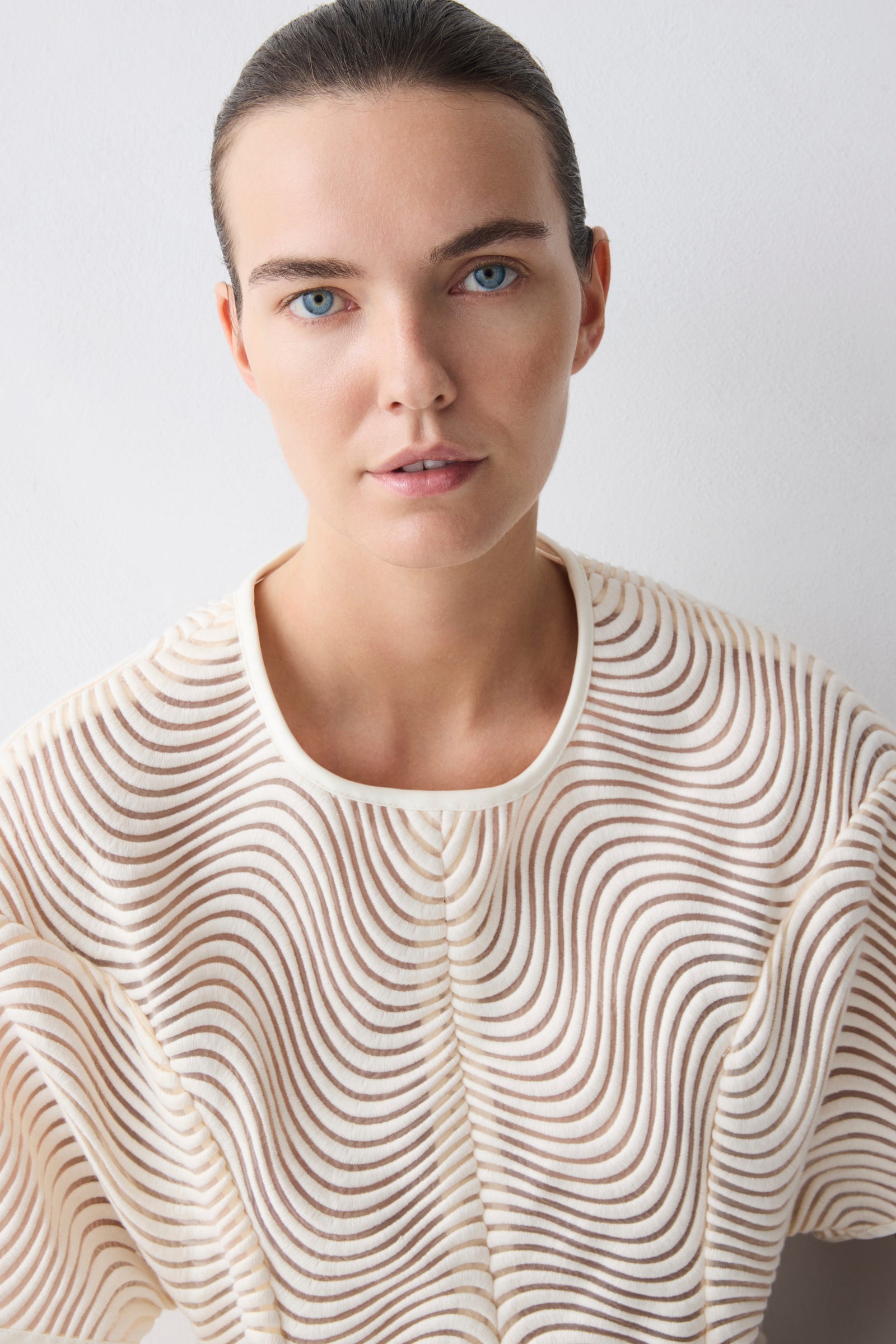 Woman wearing a beige sweater with a wavy pattern against a light background