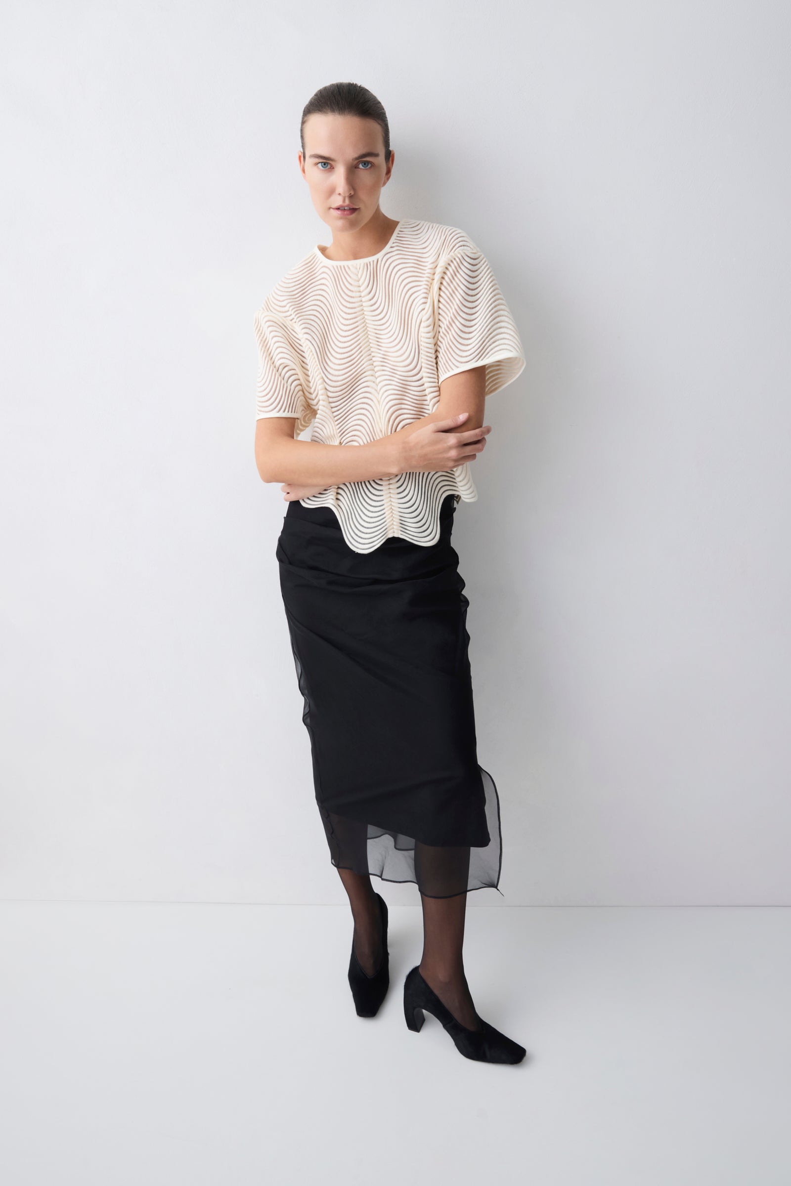 Woman wearing a beige lace top and black skirt against a white background