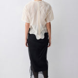 Person wearing a white blouse with a textured pattern and a black skirt on a white background