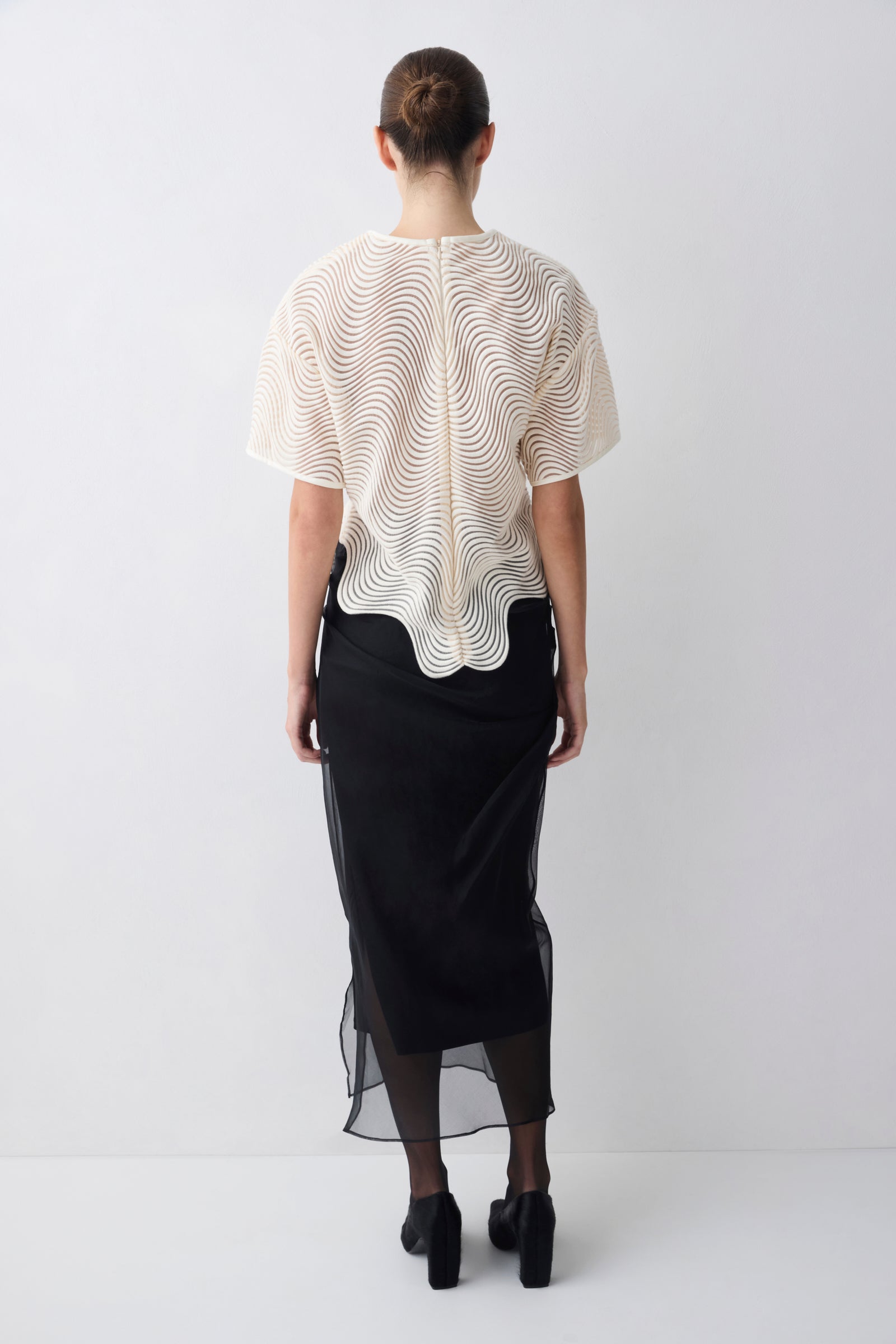 Person wearing a white blouse with a textured pattern and a black skirt on a white background