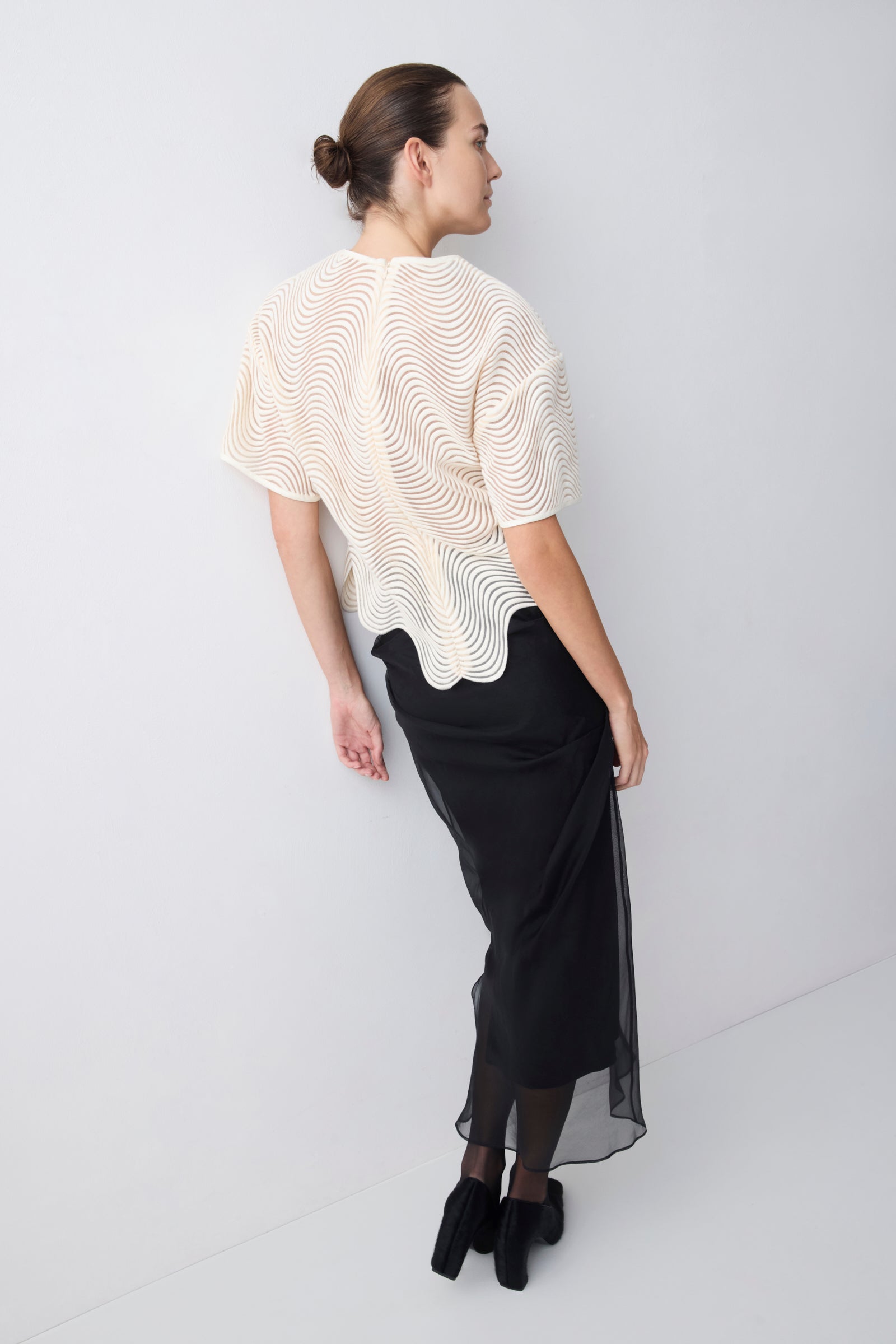 Woman wearing a white textured top and black skirt on a white background