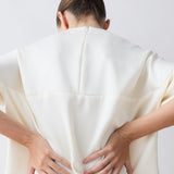 Person wearing a white garment with their back to the camera on a plain background