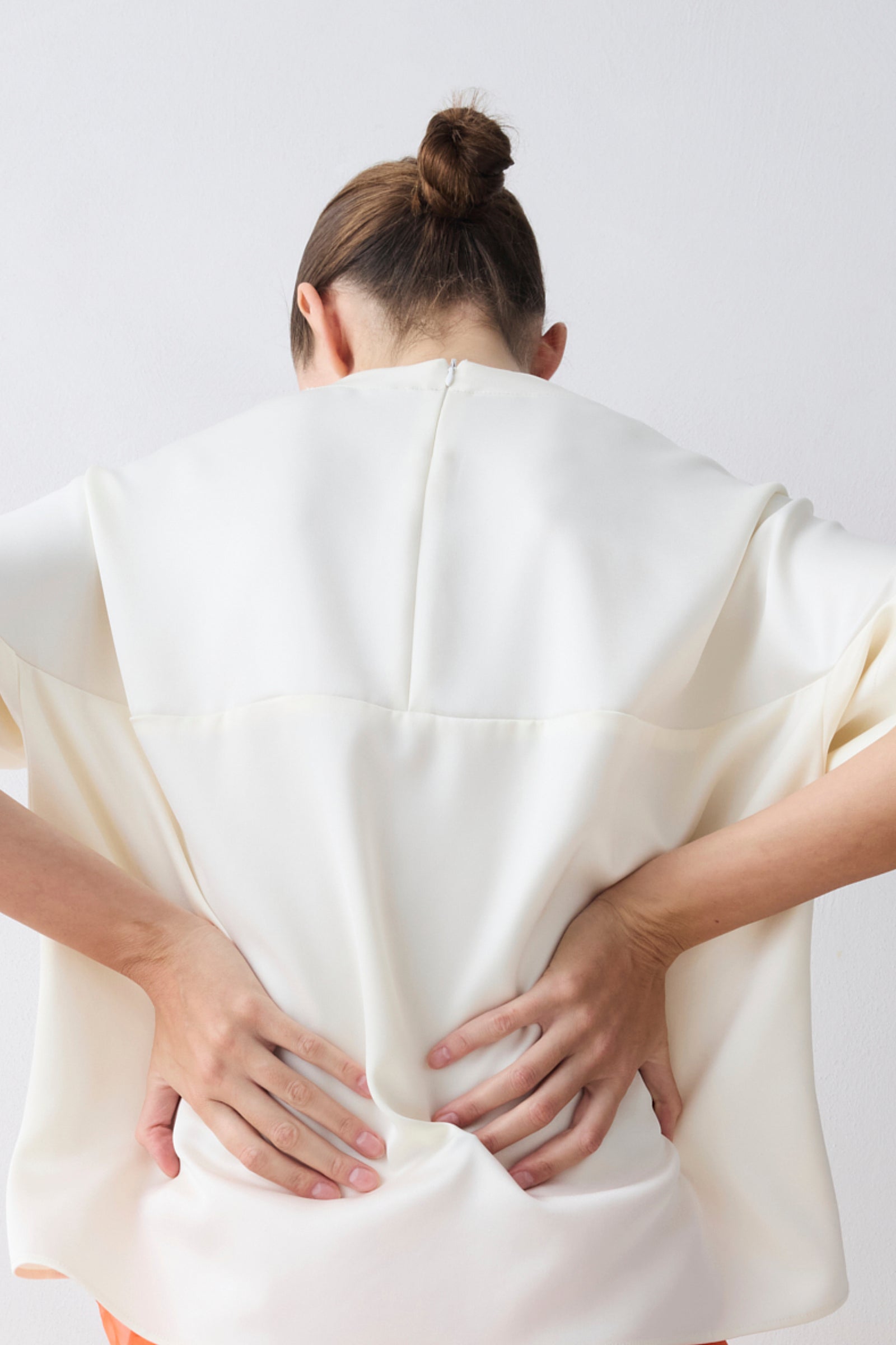 Person wearing a white garment with their back to the camera on a plain background