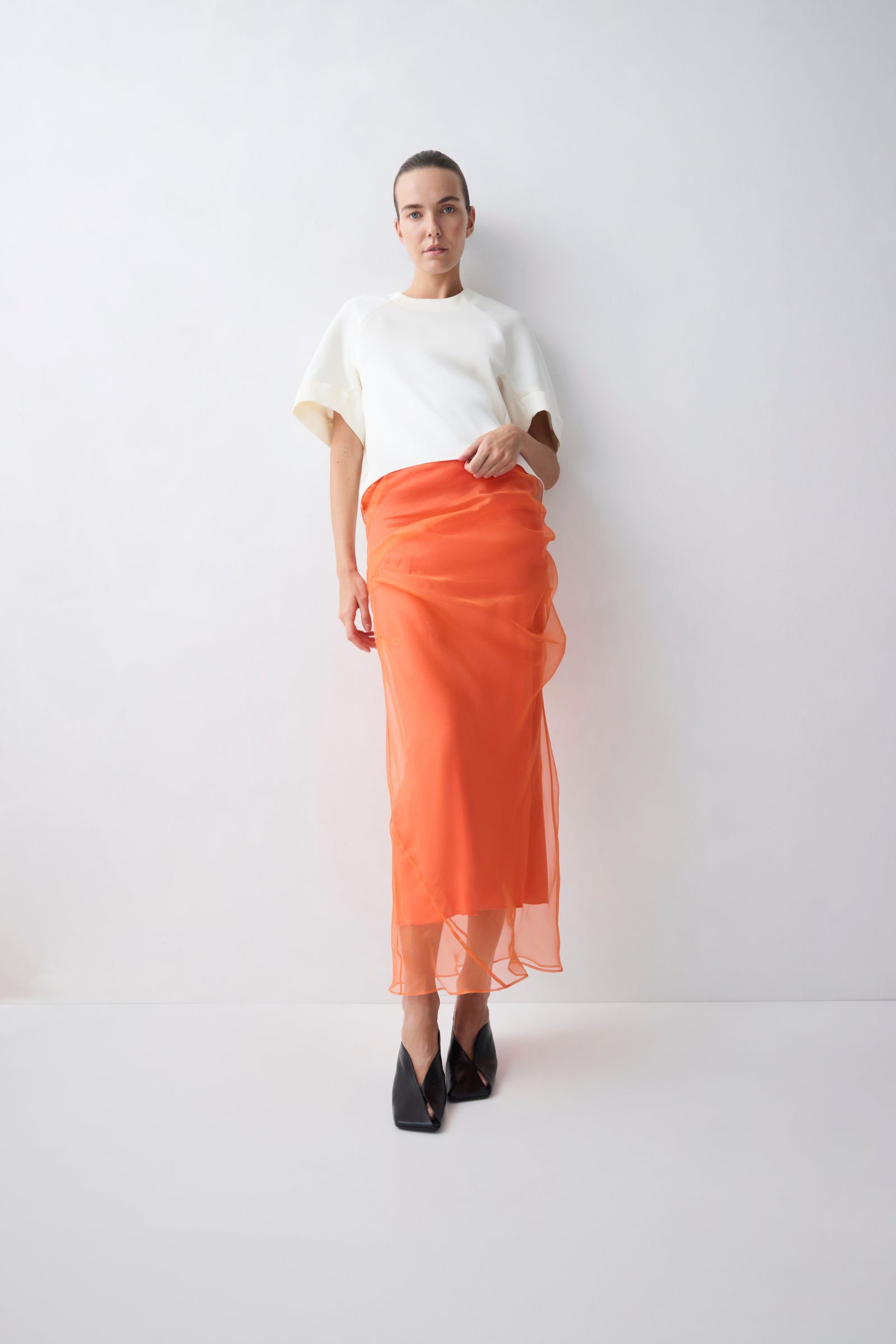 Person wearing a white top and orange skirt on a white background