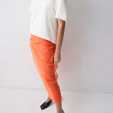 Person wearing a white top and orange pants on a plain background