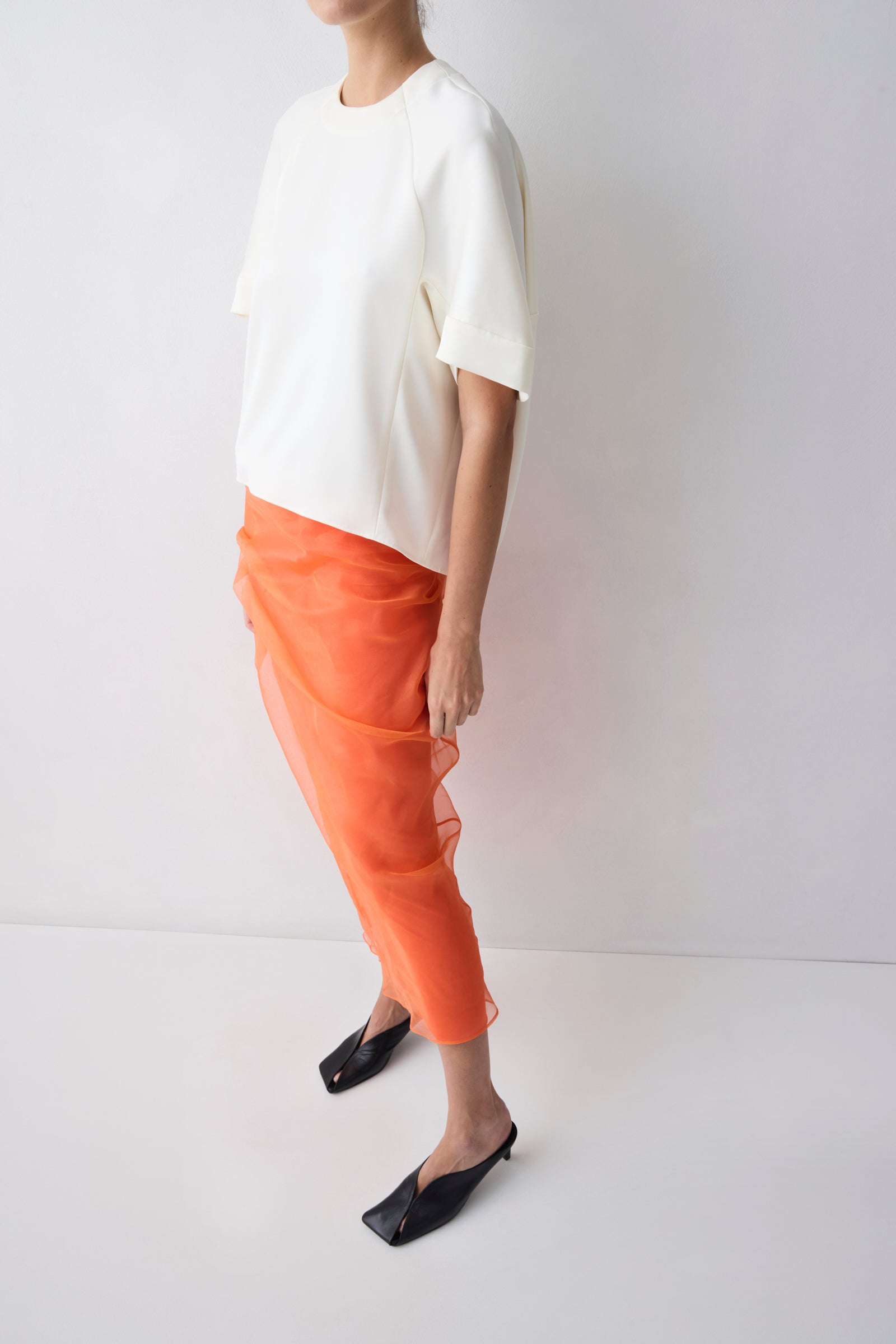 Person wearing a white top and orange pants on a plain background