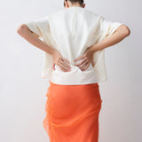 Person wearing a white top and orange skirt against a plain background
