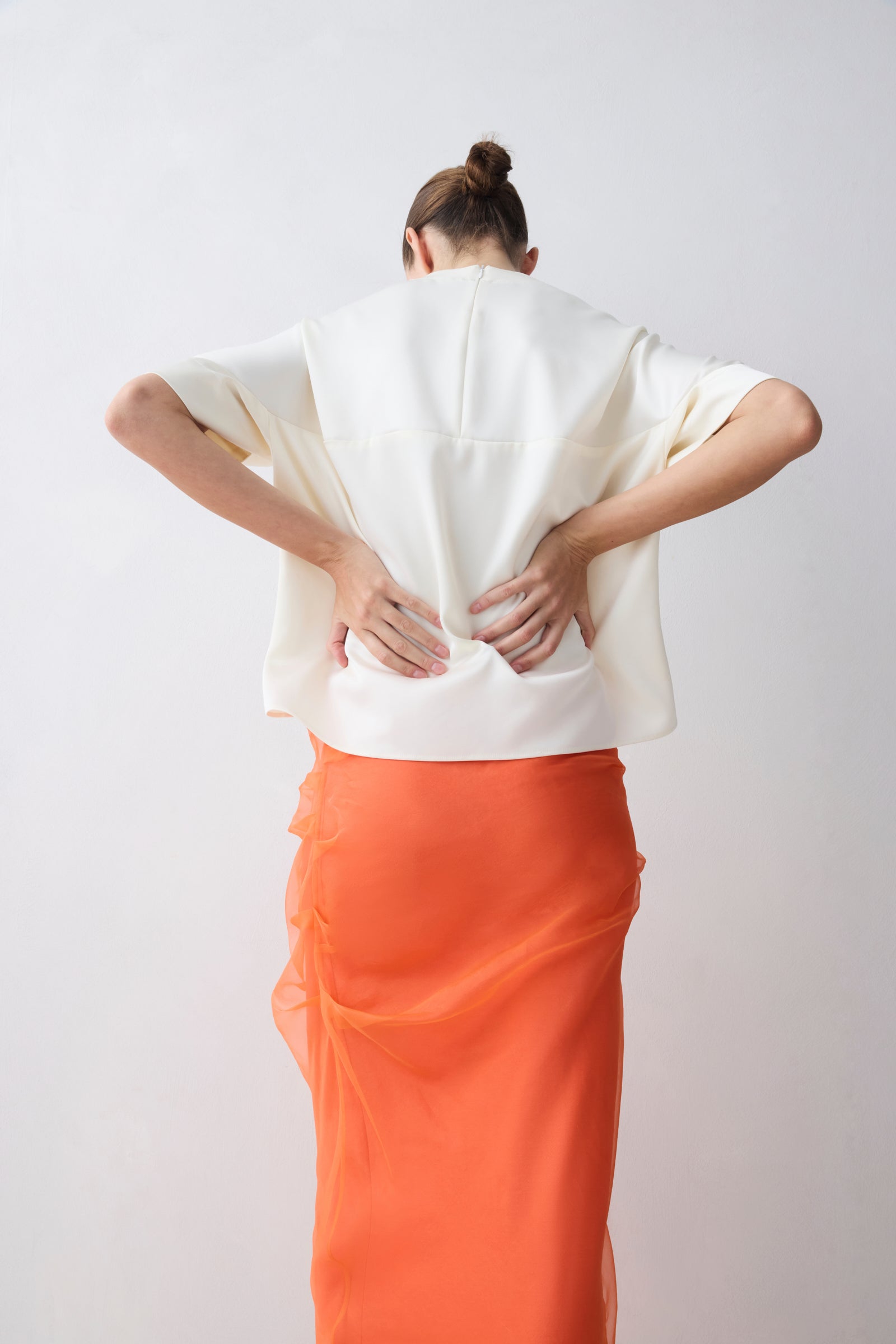 Person wearing a white top and orange skirt against a plain background