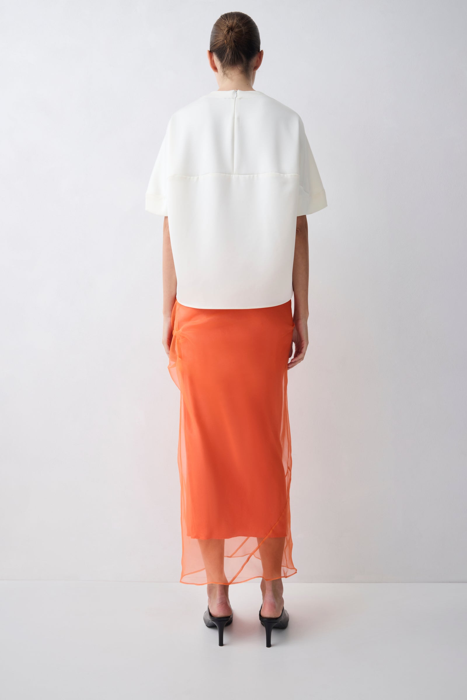 Person wearing a white top and orange skirt on a white background