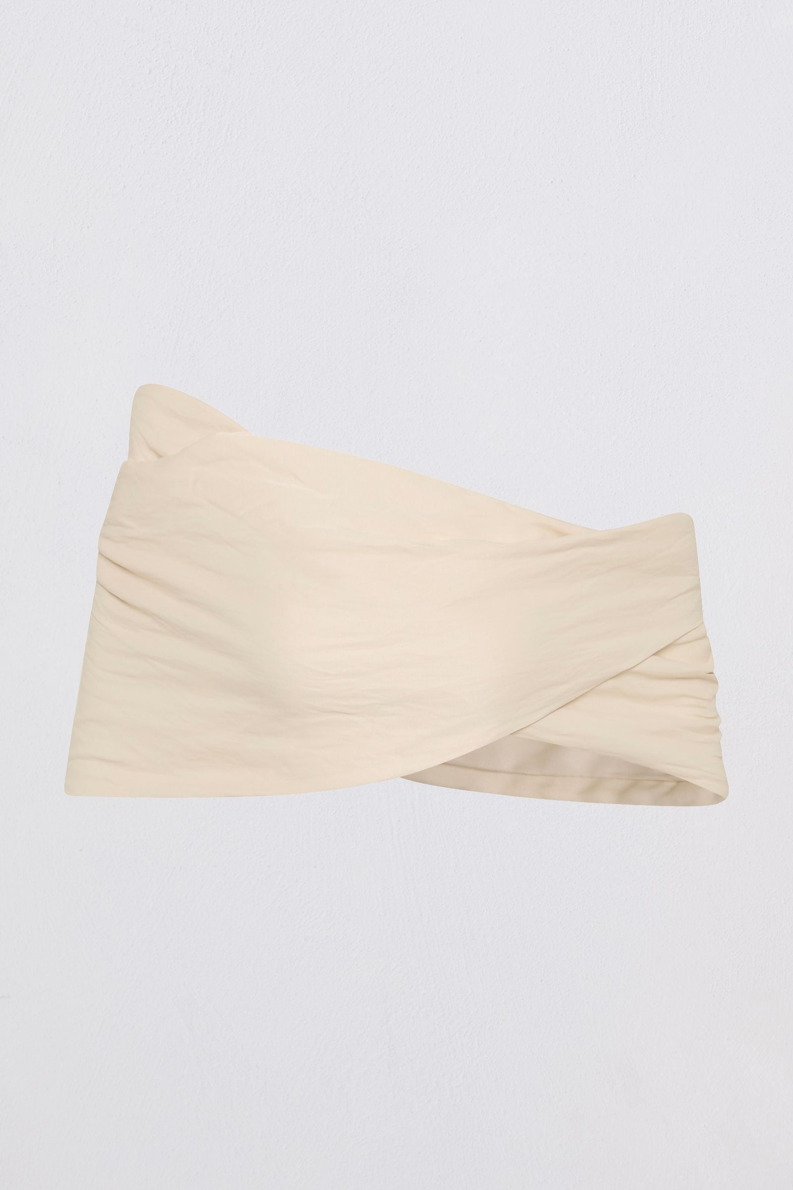 A light beige strapless bandeau top with a twisted crossover front detail, shown against a plain light gray background.