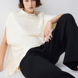 Person wearing a white top and black pants sitting on a white surface.