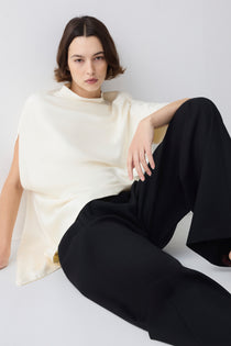 Person wearing a white top and black pants sitting on a white surface.