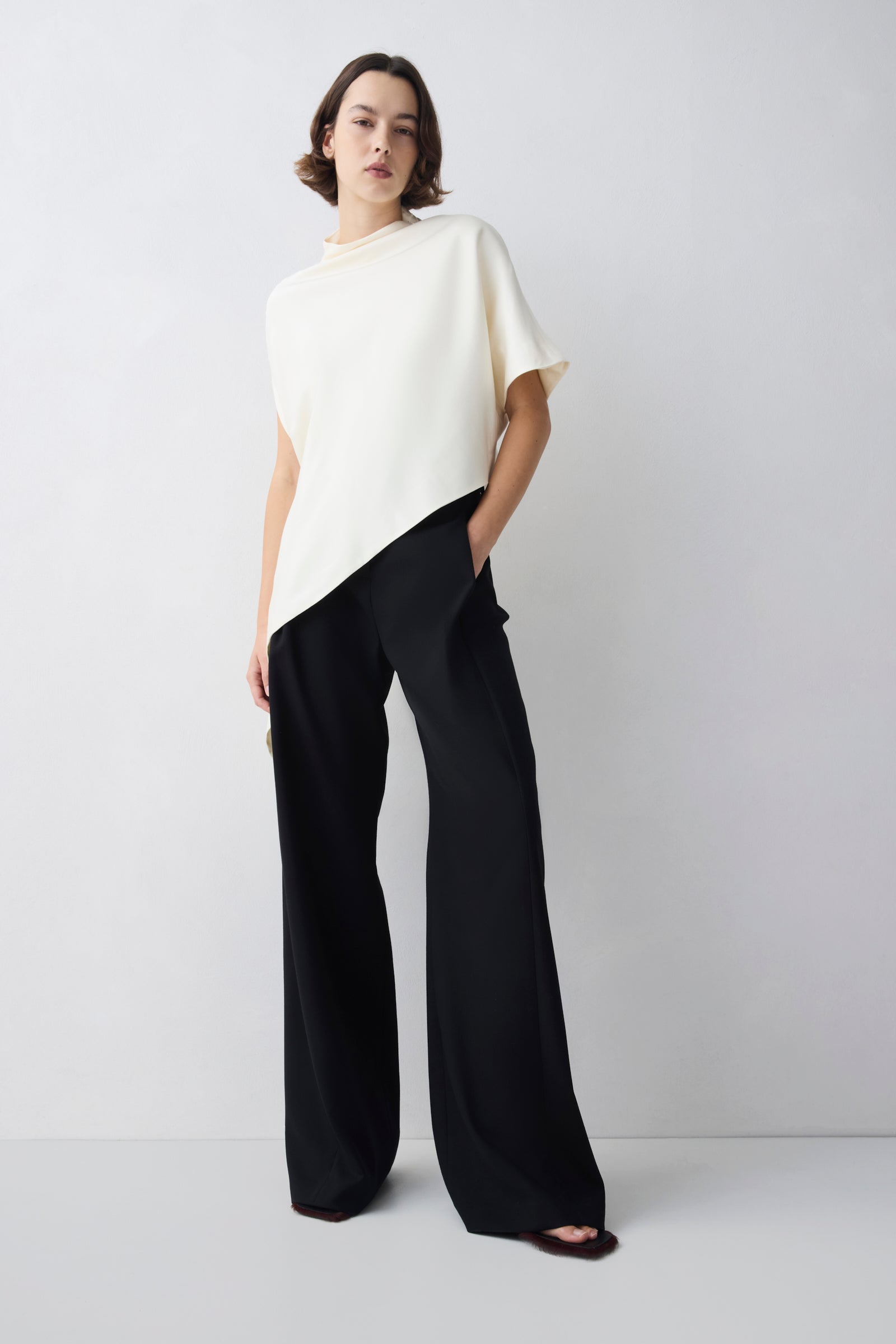 Woman wearing a white top and black pants on a plain background