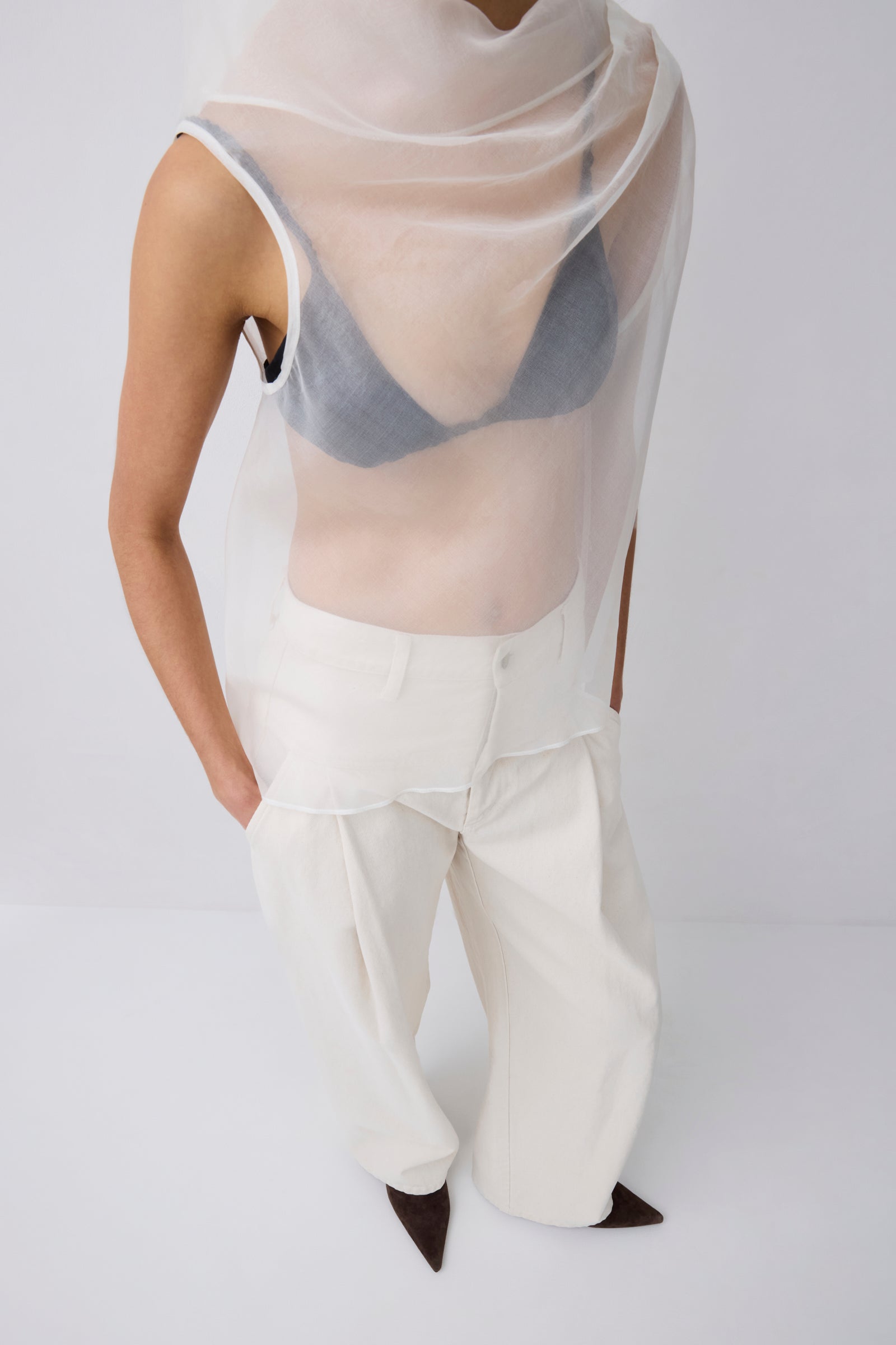 Person wearing a sheer top and white pants on a plain background