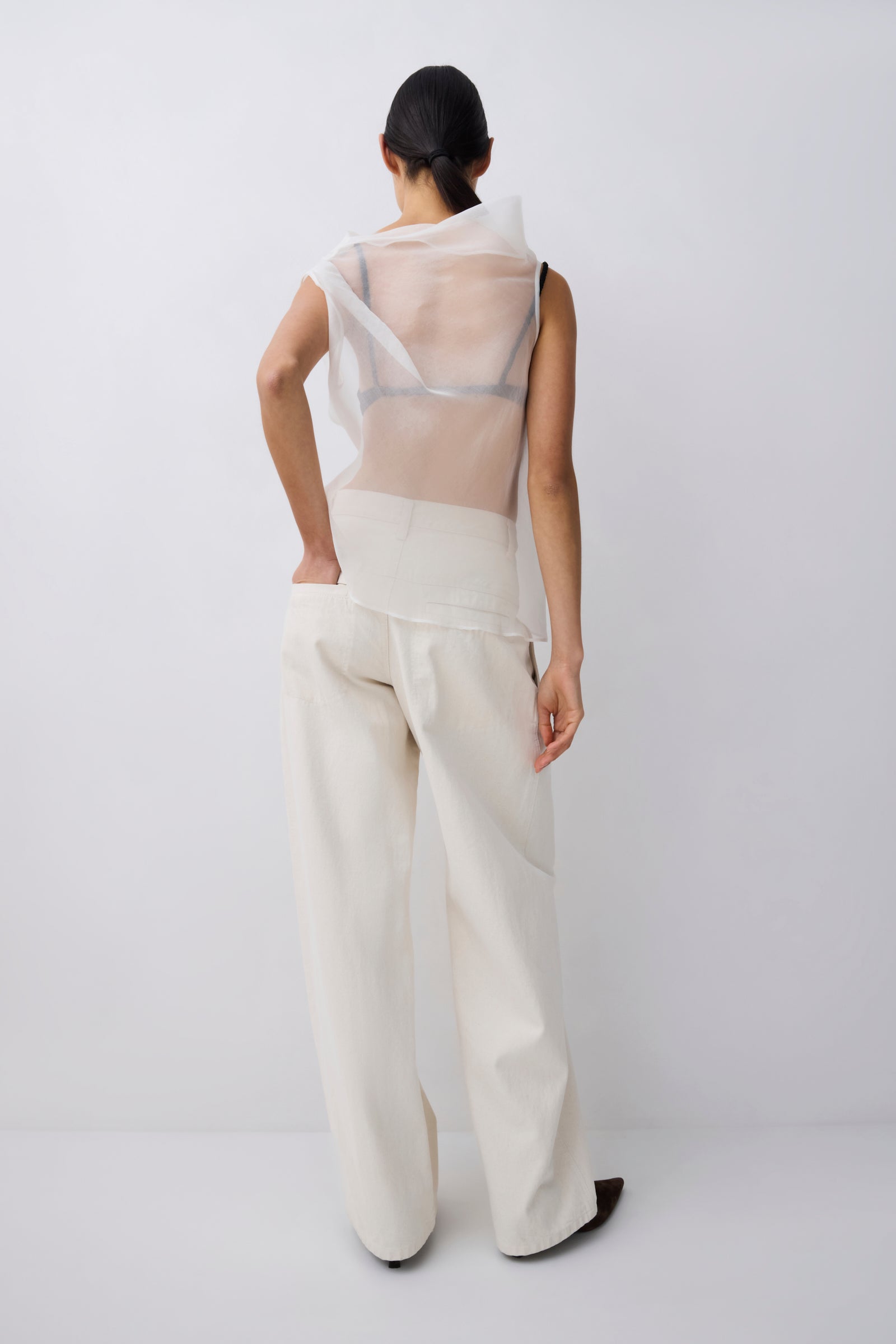 Person wearing a white outfit with sheer top on a plain background