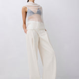 Woman wearing a sheer top and white pants on a plain background
