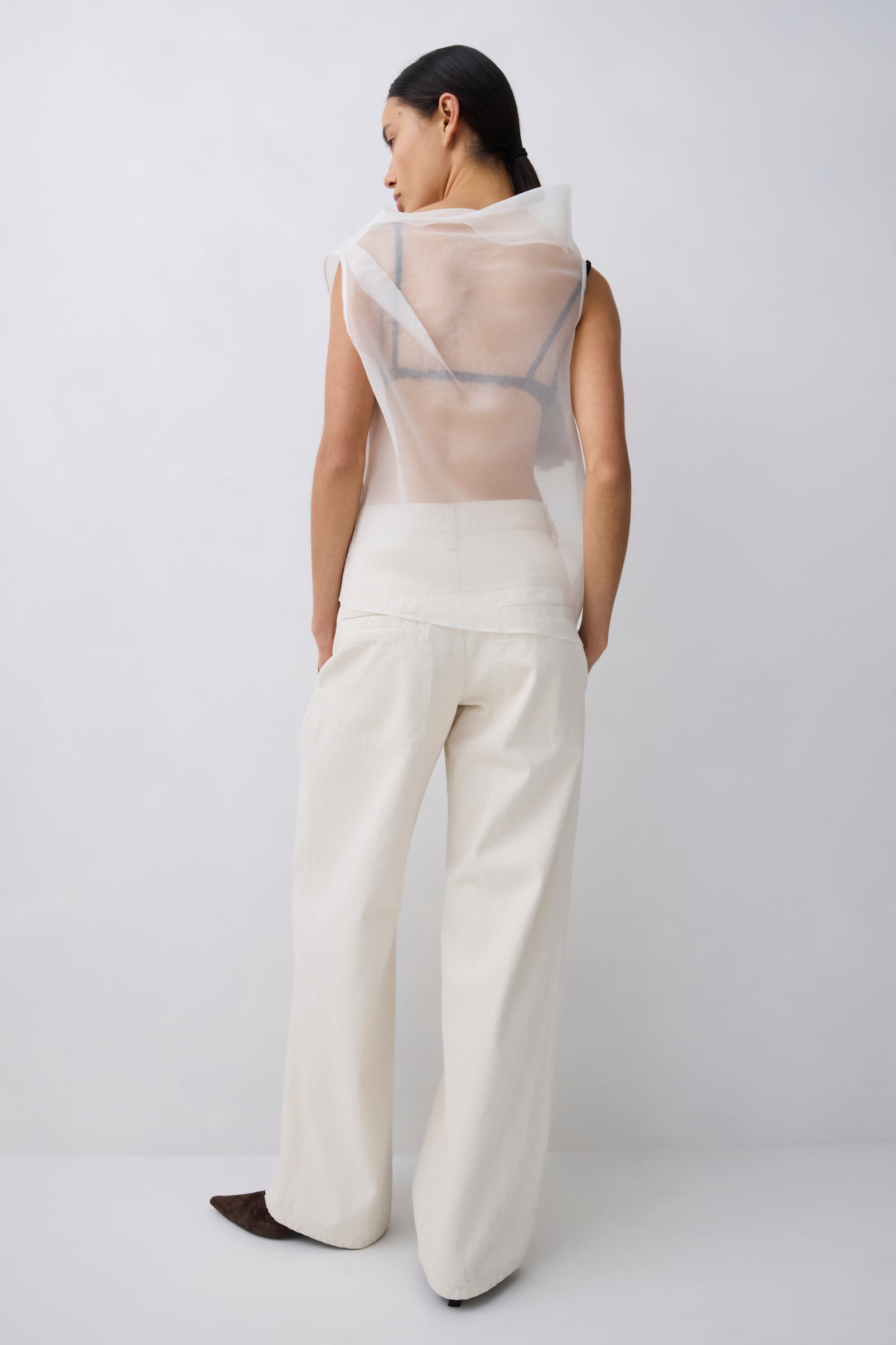 Person wearing a sheer top and white pants against a plain background