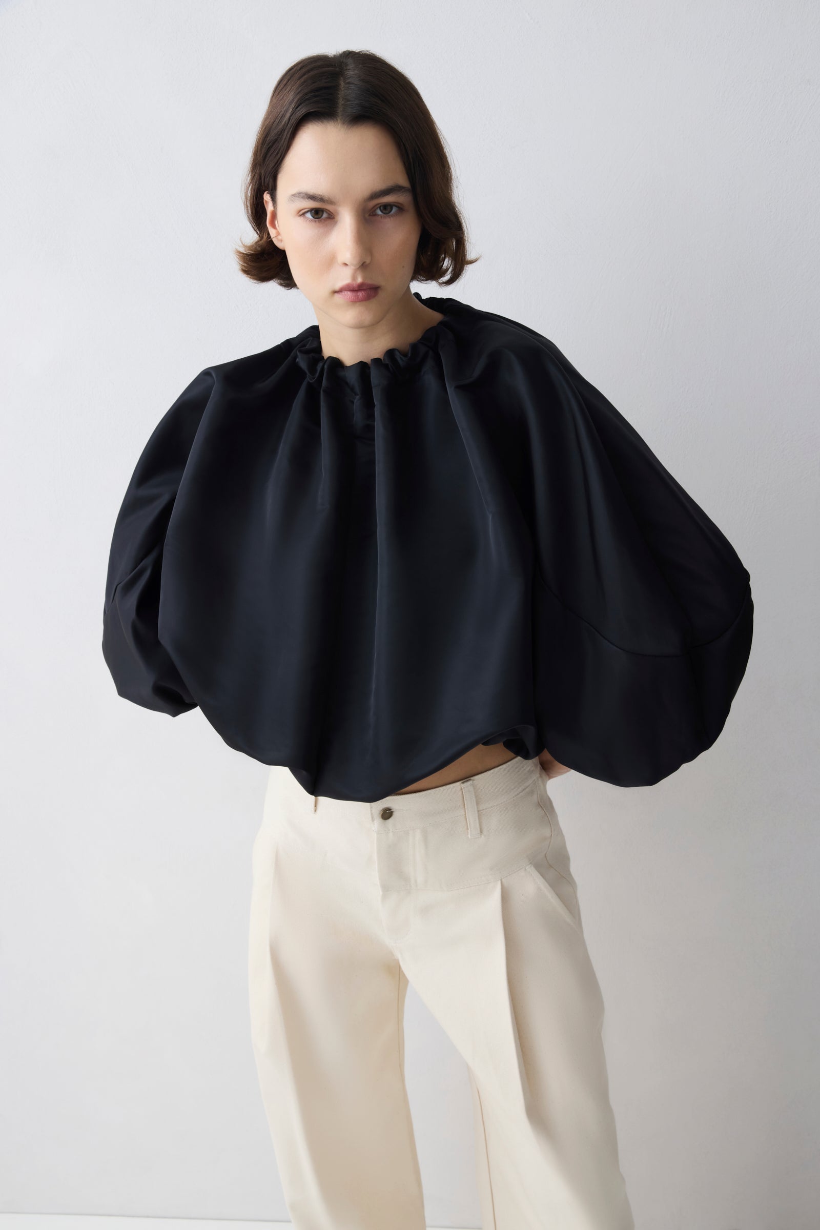 Woman wearing a black blouse with puffed sleeves and beige pants on a white background