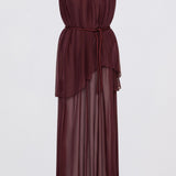 sleeveless, deep burgundy maxi dress with a tie-neck back detail, a defined waist, and a flowing layered skirt, set against a plain light gray studio background.